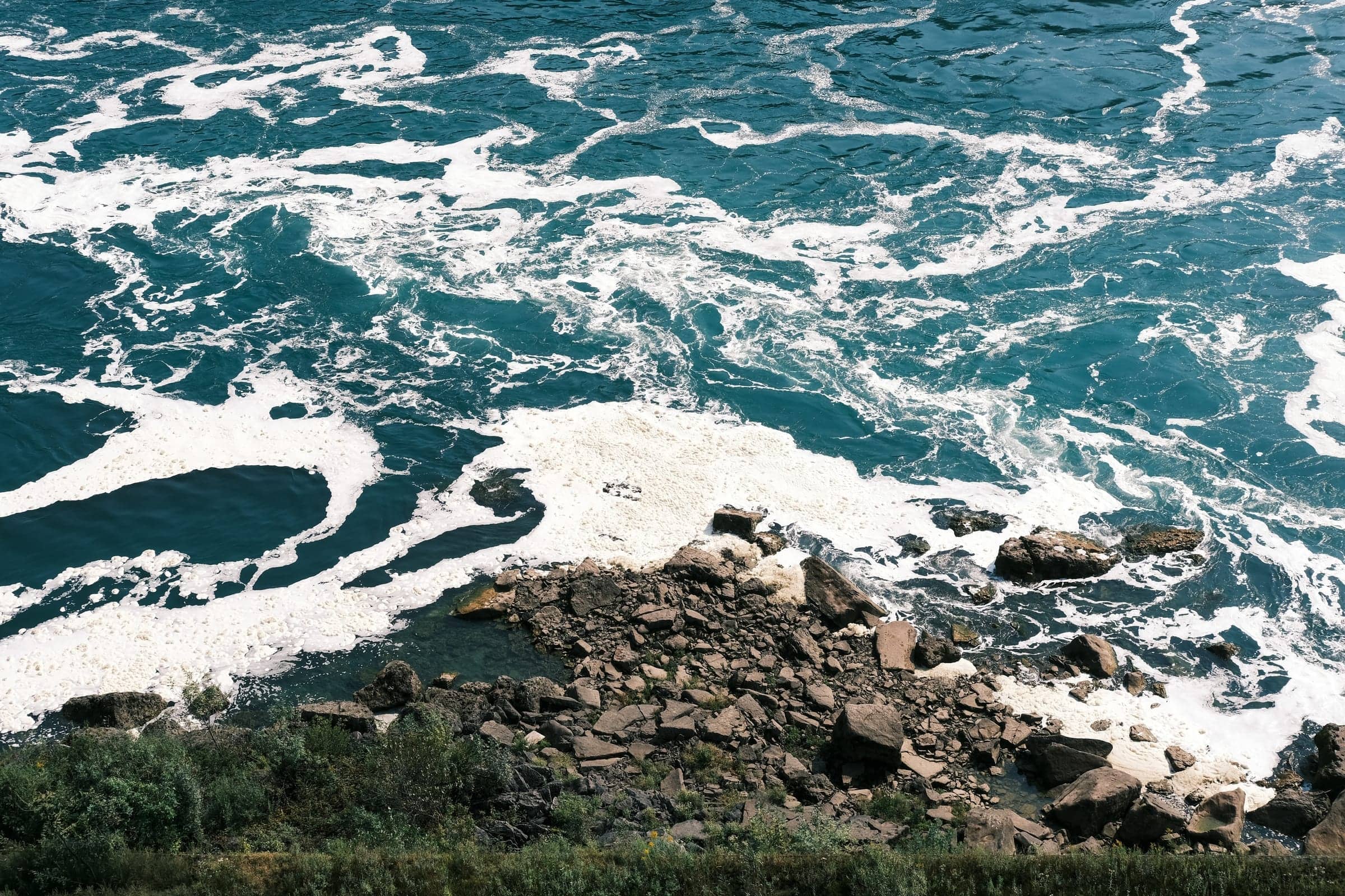 White foam swirling around dark rocks at the edge of turquoise water
